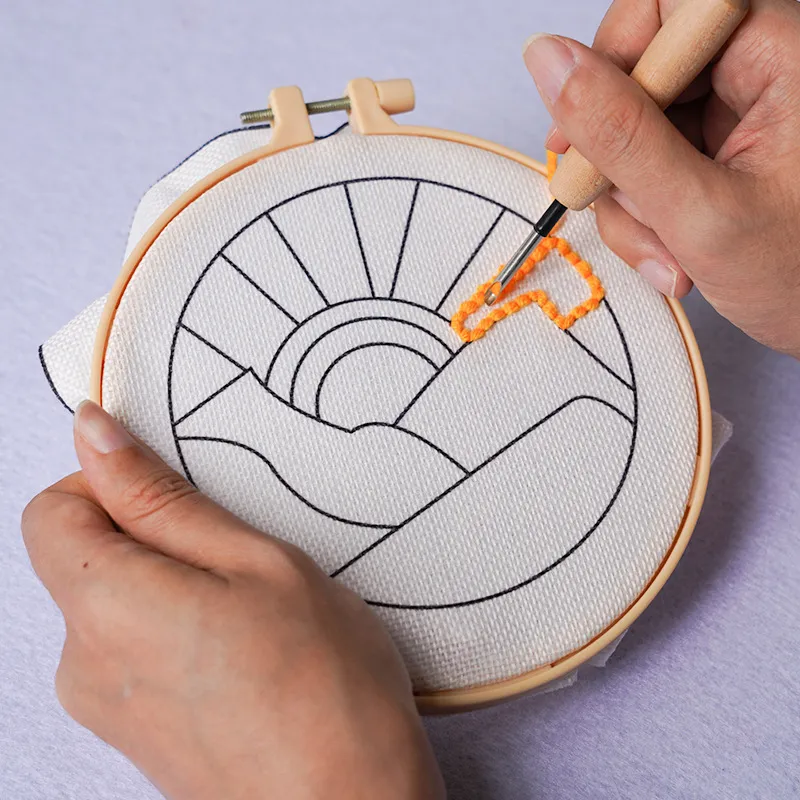 Hands working a punch needle through the printed landscape fabric in a hoop